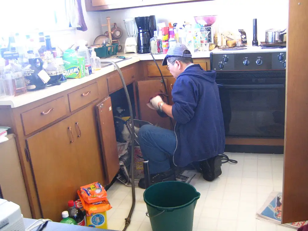Fontanero reparando una tubería bajo el fregadero de una cocina