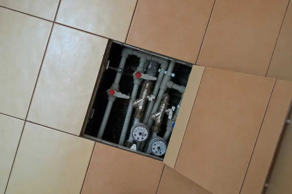 Registro abierto en la pared de un baño con dos contadores de agua y sus llaves de paso